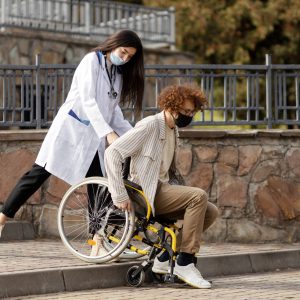 Nice nurse helps a patient in a wheelchair down the stairs. Assistance to a disabled patient.